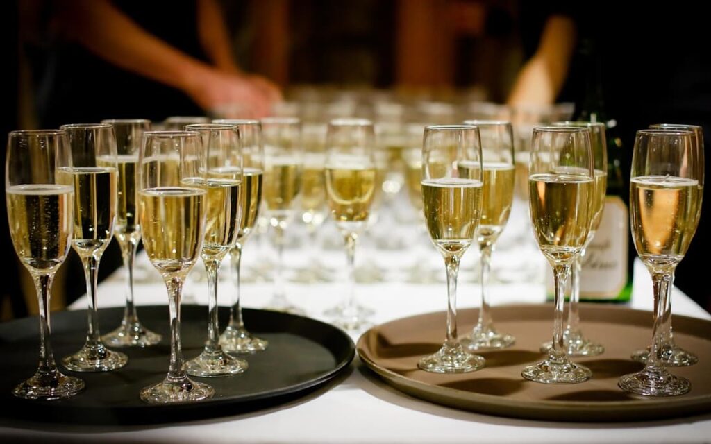 Alt: Rows of champagne glasses on a serving tray, prepared for a celebration
