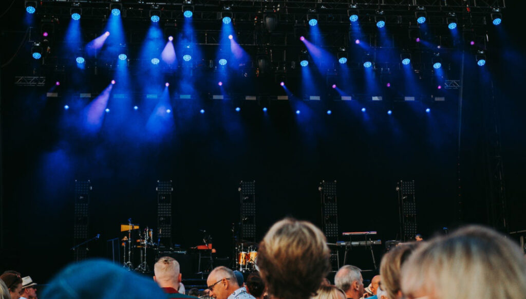 Audience from behind looking towards a stage with blue lights before a concert