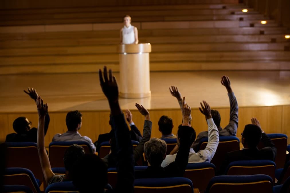 An audience raising hands to ask questions in a conference hall