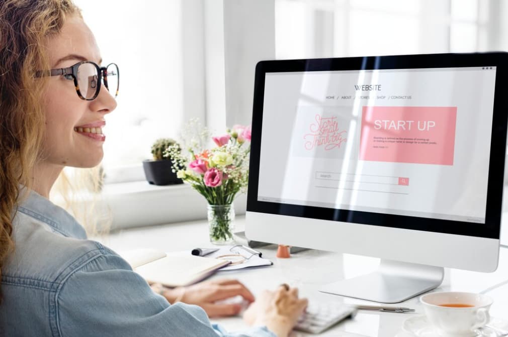 A smiling woman working on an iMac with a startup screen