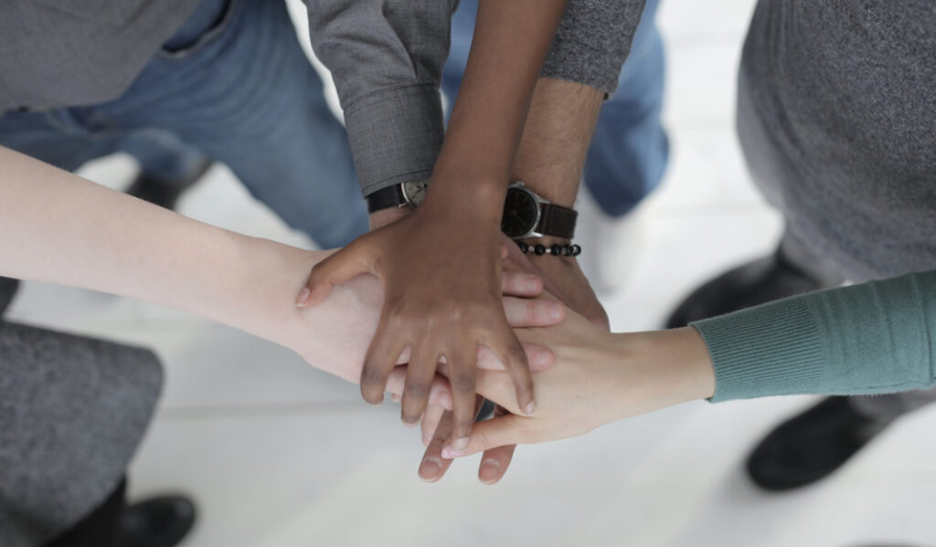 An overhead view of several people's hands stacked on top of each other in a gesture of unity or teamwork