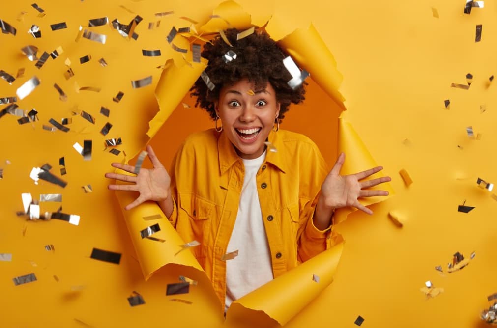 A joyful person bursting through a yellow paper wall with confetti