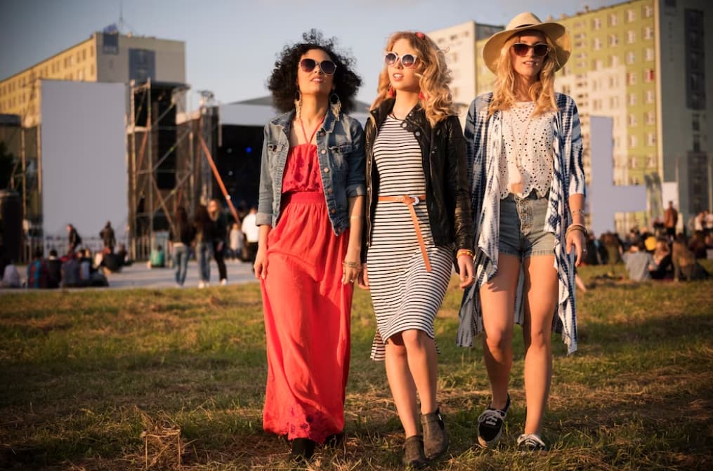 Three friends in chic festival attire enjoy a sunny outdoor event