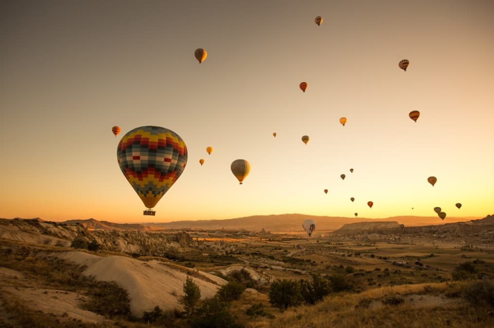 Hot air balloons float in a golden sunrise sky over a rugged landscape